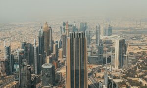 Aerial view of Dubai's skyline with high-rise buildings and iconic skyscrapers, set against a hazy sky, showcasing the modern architectural landscape of the city.