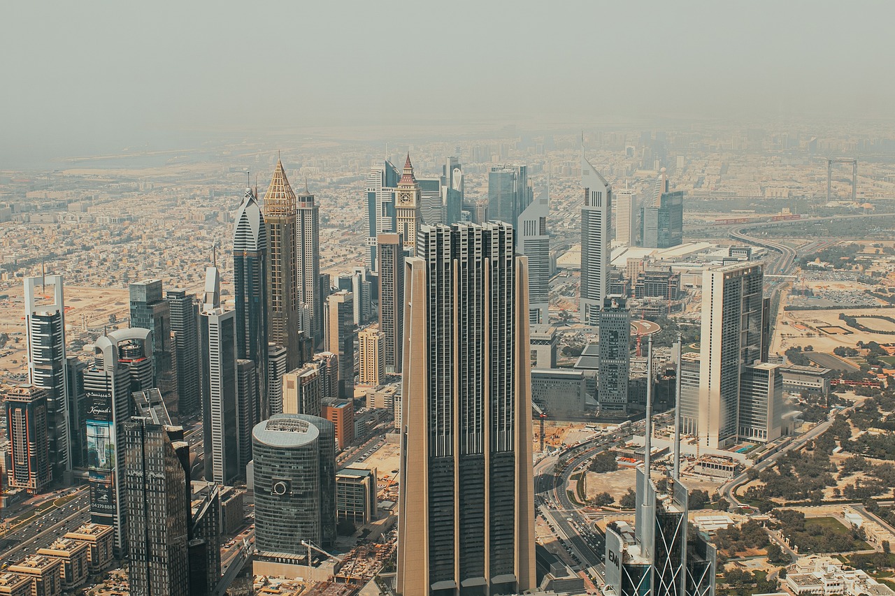 Aerial view of Dubai's skyline with high-rise buildings and iconic skyscrapers, set against a hazy sky, showcasing the modern architectural landscape of the city.