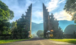 Entrance to a luxury resort in Bali, with traditional Balinese gate structures, lush green landscape, and a serene, tropical backdrop under a bright blue sky.