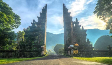 Entrance to a luxury resort in Bali, with traditional Balinese gate structures, lush green landscape, and a serene, tropical backdrop under a bright blue sky.