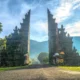 Entrance to a luxury resort in Bali, with traditional Balinese gate structures, lush green landscape, and a serene, tropical backdrop under a bright blue sky.