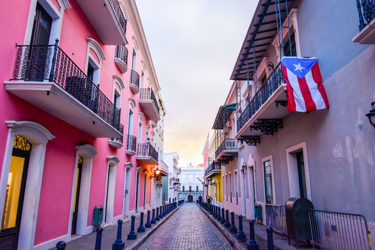 Street in puerto rico with pink builiding and flag hanging from balcony