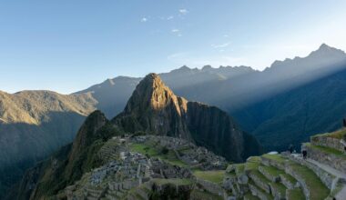 A scenic view of Machu Picchu, an ancient Incan citadel located high in the Andes Mountains of Peru, with green terraces, rugged peaks, and a clear blue sky in the background.