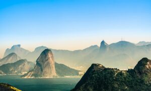 A breathtaking aerial view of Rio de Janeiro, showcasing its iconic mountains, lush greenery, and the serene coastline under a clear blue sky.