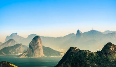 A breathtaking aerial view of Rio de Janeiro, showcasing its iconic mountains, lush greenery, and the serene coastline under a clear blue sky.