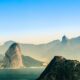 A breathtaking aerial view of Rio de Janeiro, showcasing its iconic mountains, lush greenery, and the serene coastline under a clear blue sky.