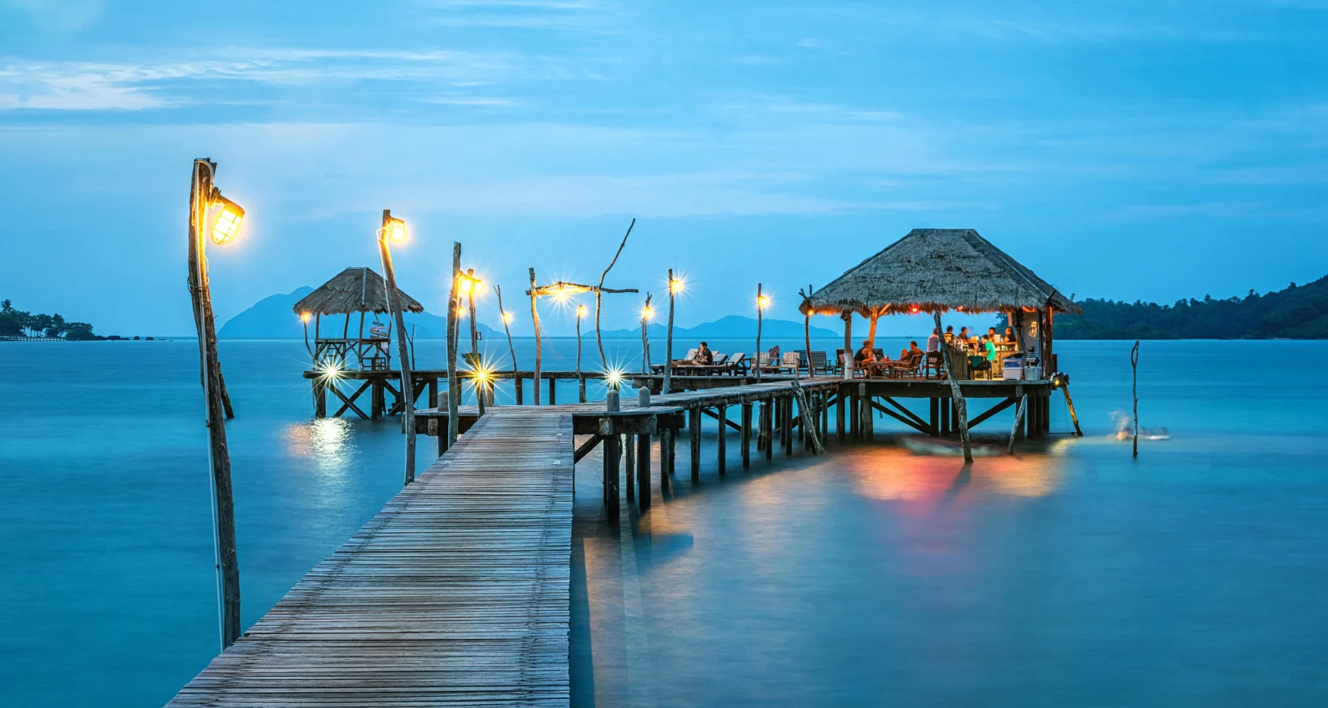 A serene tropical scene featuring a wooden pier extending over calm, turquoise water.