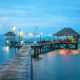 A serene tropical scene featuring a wooden pier extending over calm, turquoise water.